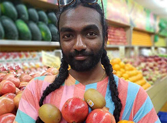 Dhanesh Krishnarao holding an armful of fruit in a grocery store