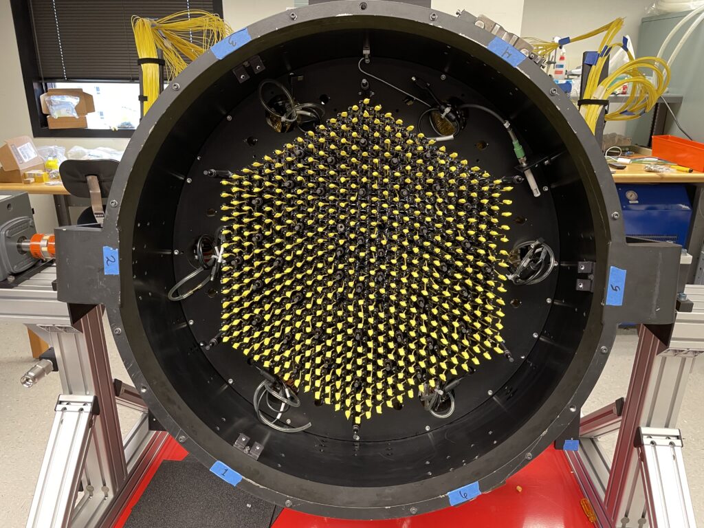 Inside a circular housing sits a hexagonal array of regularly-spaced optical fibers with yellow caps on the end of each.